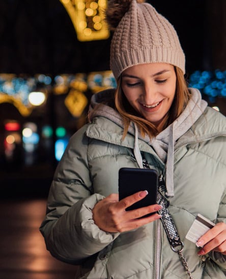 Woman on festive street shopping on phone with credit card