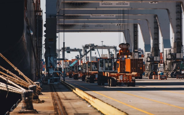 Shipping containers stacked at port with many freight trucks exiting